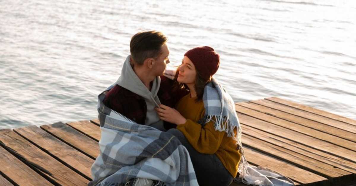 Na foto, um casal se encontra à beira do pier, trocando olhares carregados de amor enquanto pensam: "Quantas Vezes um Casal Normal Faz Amor Por Dia?"
